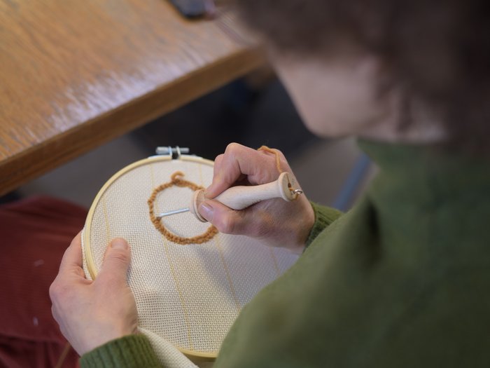 Workshop di “Punch Needle” alla VHS Südtirol: la creatività si unisce alla tradizione Persona che ricama con la tecnica punch needle su stoffa in telaio