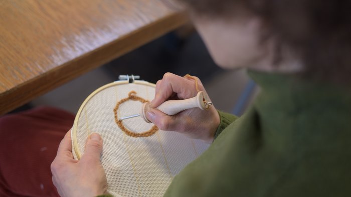 „Punch Needle“ Workshop an der VHS Südtirol: Kreativität und Tradition vereint Person beim Sticken mit Punch-Needle-Technik auf Stoff im Stickrahmen