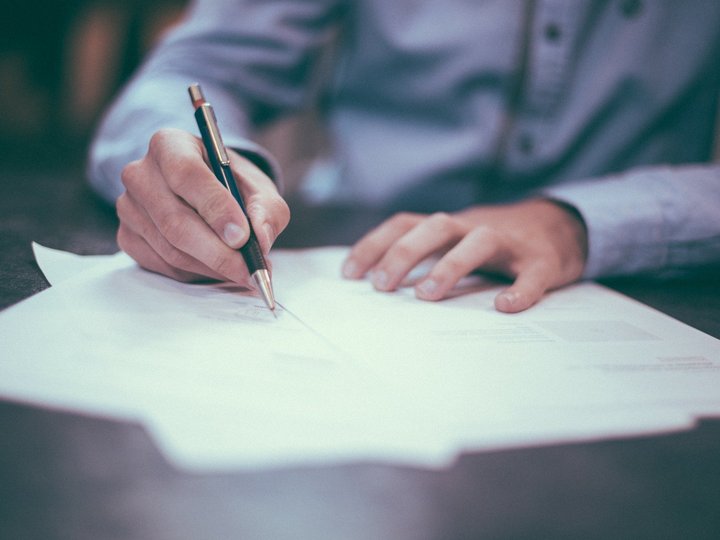 Fakten zum Thema Hand unterschreibt Dokument mit schwarzem Stift auf Tisch