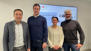 News Vier Personen stehen vor einem Bildschirm in einem modernen Büro