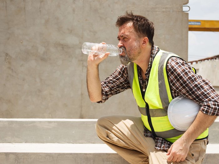 Le misure contro il caldo nei cantieri sono importanti e vengono prese sul serio Operaio edile con giubbotto riflettente che beve acqua e tiene casco bianco