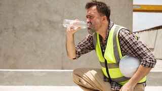 News Bauarbeiter in Warnweste trinkt Wasser und hält weißen Helm