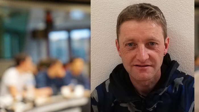 „Macht eure Leute glücklich“ Porträt eines lächelnden Mannes vor verschwommenem Hintergrund mit Menschen