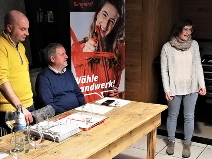 Handwerk: Tradition schafft Zukunft Drei Personen bei Tisch mit Dokumenten, eine Frau steht und spricht, Werbebanner im Hintergrund