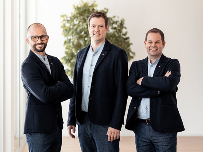 lvh.apa feiert 75jähriges Jubiläum Drei Männer in Anzügen stehen nebeneinander in einem modernen Büro