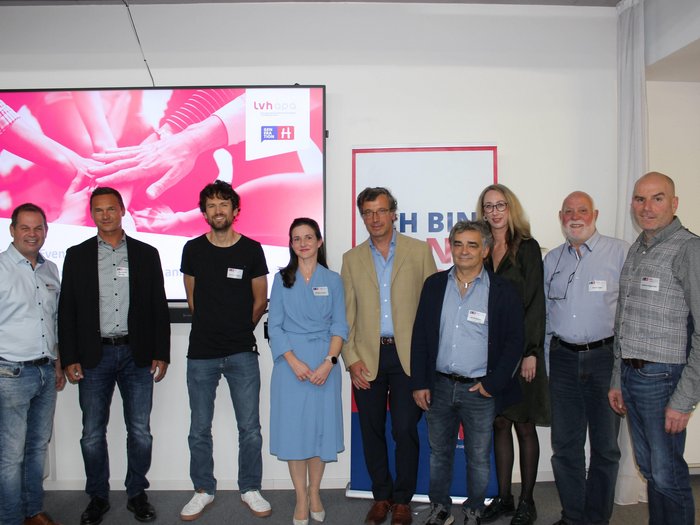 Evento tessile Nove persone in piedi davanti a uno schermo e a un cartellone a un evento.