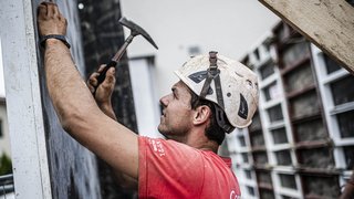 © Hannes Niederkofler Bauarbeiter mit Helm, der mit Hammer an einer Wand arbeitet
