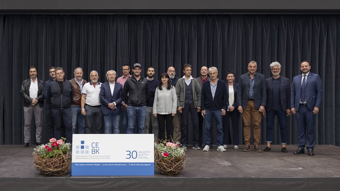 Cassa Edile della Provincia Autonoma di Bolzano: premiazione iscritti “30 anni di fiducia“ Gruppo di 18 persone su palcoscenico con cartello anniversario 30 anni CE BK