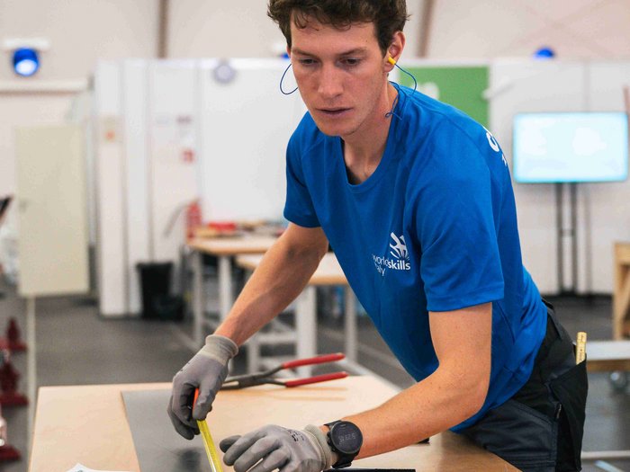 EuroSkills 2023: adesso bisogna concentrarsi! Giovane uomo misura lastra di metallo con metro in laboratorio