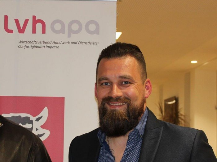 Rinnovato il Contratto Collettivo Nazionale per il settore Alimentare-Panificazione Uomo sorridente con barba davanti a un banner dell'associazione economica artigianato e servizi