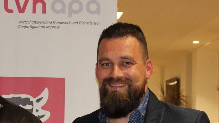 Rinnovato il Contratto Collettivo Nazionale per il settore Alimentare-Panificazione Uomo sorridente con barba davanti a un banner dell'associazione economica artigianato e servizi