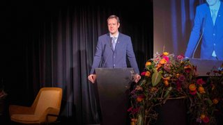 News Mann im Anzug hält eine Rede an einem mit Blumen geschmückten Podium