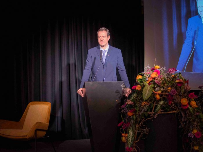 “Artigiani. Mani e Cuore” Uomo in abito parla a un podio decorato con fiori colorati