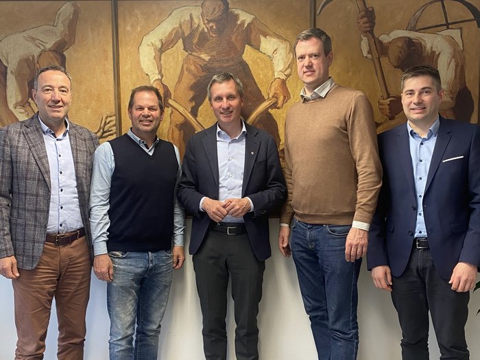 Erstes Treffen der lvh-Spitze mit Landesrat Luis Walcher Fünf Männer in Geschäftskleidung vor Wandgemälden mit Arbeitsszenen