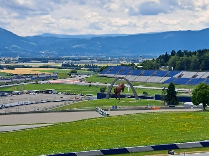 Viaggio culturale nel Burgenland – Opera e musical come fulcro del programma Circuito automobilistico in paesaggio collinare con statua di bisonte e cielo nuvoloso