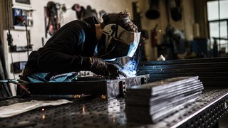 News Schweißer mit Schutzhelm arbeitet an Metallstück in Werkstatt