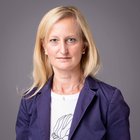 Birgit Gruber Ritratto di donna bionda con giacca blu scuro su sfondo grigio