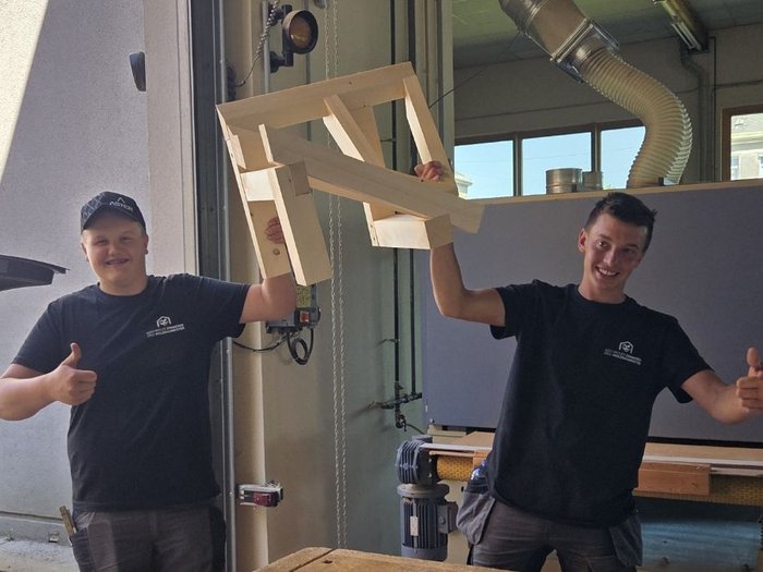 Wenn Holz Zukunft baut Zwei Männer in Werkstatt halten einen Holzstuhl und zeigen Daumen hoch