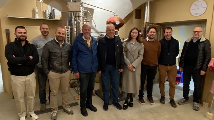 Riunione del gruppo comunale Brunico di lvh.apa: progetti promettenti e forte collaborazione Gruppo di dieci persone in una stanza con impianto di distillazione sullo sfondo