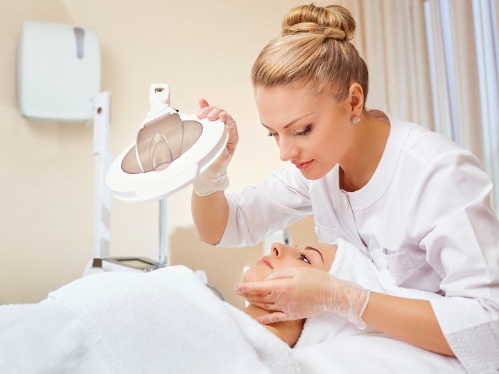 Ausbildung Kosmetikerin untersucht Gesicht einer Frau mit Lupe in einem Spa