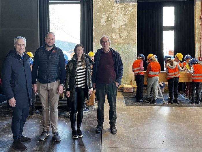 Erstmals in Schlanders! Die „Erlebniswelt Baustelle“ Vier Erwachsene stehen in einer Halle, im Hintergrund arbeiten Kinder mit Schutzhelmen und Warnwesten