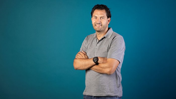 „Eine starke Interessenvertretung erfordert eine aktive Beteiligung aller“ Mann in grauem Polohemd steht vor blauem Hintergrund mit verschränkten Armen