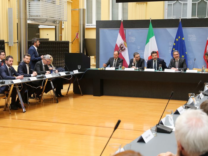Brenner - Handelskammern von Bozen und Trient sowie die Transportverbände: Die Tiroler Fahrverbote sind längst überholt Politische Sitzung mit Teilnehmern und Flaggen von Südtirol, Italien, EU