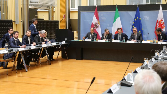 Brenner - Handelskammern von Bozen und Trient sowie die Transportverbände: Die Tiroler Fahrverbote sind längst überholt Politische Sitzung mit Teilnehmern und Flaggen von Südtirol, Italien, EU