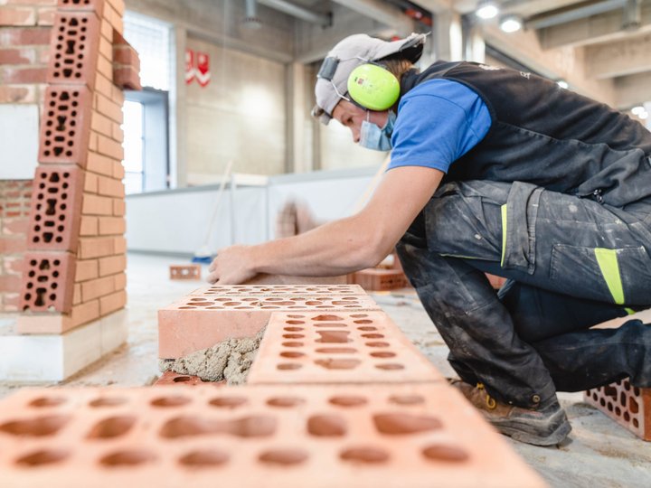 Baumeister und Maurer Maurer setzt Ziegelsteine mit Mörtel in einer Werkstatt