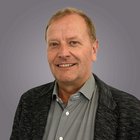 Gründung und Nachfolge Porträt eines lächelnden Mannes mit hellem Haar vor grauem Hintergrund