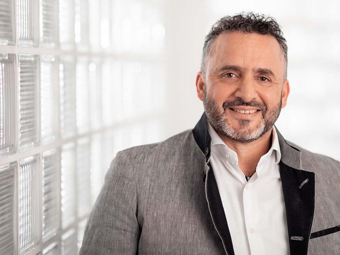 Schritt für Schritt wieder Arbeit aufnehmen Porträt eines lächelnden Mannes mit grauem Anzug und weißem Hemd vor Glasscheibenwand