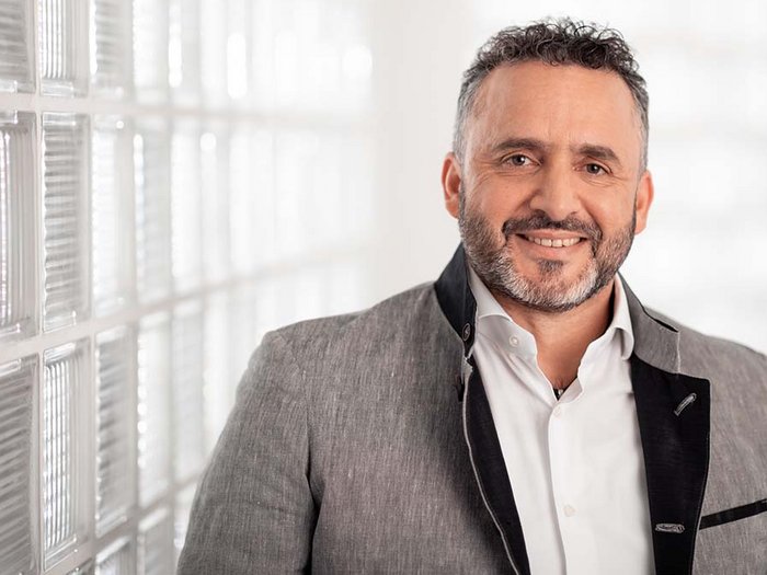 Gruber: „Jetzt klaren Kopf bewahren“ Porträt eines lächelnden Mannes mit grauem Anzug und weißem Hemd vor Glasscheibenwand