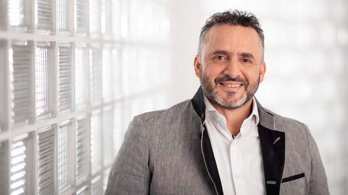 Schritt für Schritt wieder Arbeit aufnehmen Porträt eines lächelnden Mannes mit grauem Anzug und weißem Hemd vor Glasscheibenwand