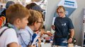 WorldSkills Italy: Junge Talente im Wettkampf Frau erklärt Kindern ein technisches Gerät auf einer Messe
