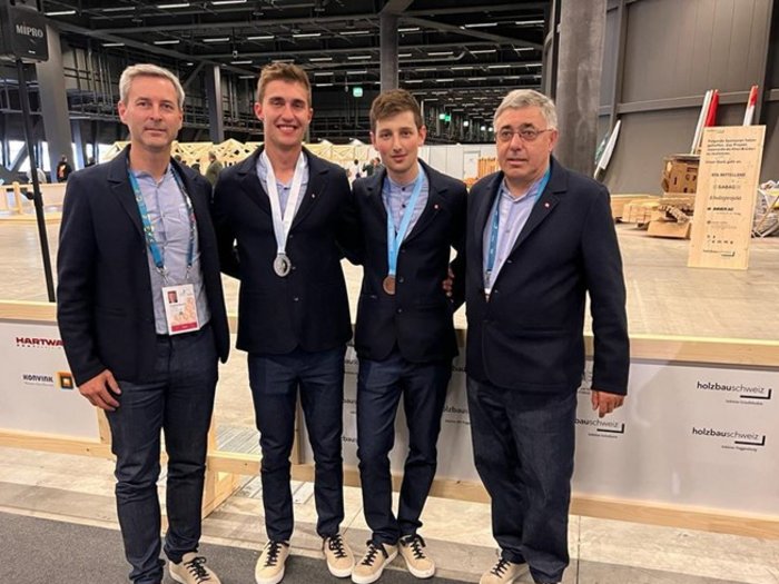 WorldSkills 2022 Special Edition: Zimmerer Marcel Bolego holt Silbermedaille Vier Männer posieren bei einer Veranstaltung, zwei tragen Medaillen