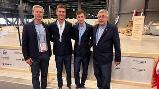 News Vier Männer posieren bei einer Veranstaltung, zwei tragen Medaillen