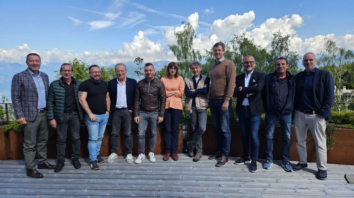 L’artigianato a sostegno di lavoratori e famiglie Dodici persone in piedi su una terrazza di legno con alberi e montagne sullo sfondo