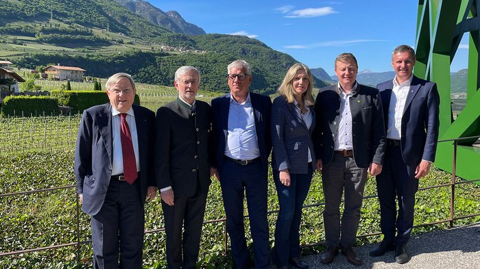 Stabübergabe im Handwerk in Klausen Sechs Personen posieren vor Berglandschaft und klarem Himmel