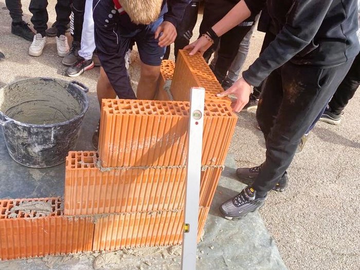 I giovani scoprono le professioni nei settori dell’artigianato e dell’ospitalità Adolescenti costruiscono muro con mattoni usando una livella