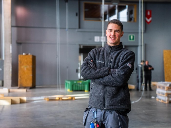 Appiano Produktiv: tre giorni all’insegna dell’economia regionale Giovane uomo con giacca da lavoro grigia sorride in capannone industriale