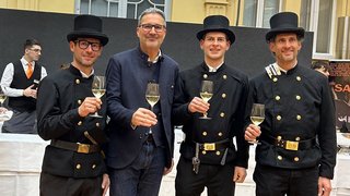 News Vier Männer, drei in Schornsteinfeger-Uniform, stoßen mit Weingläsern an