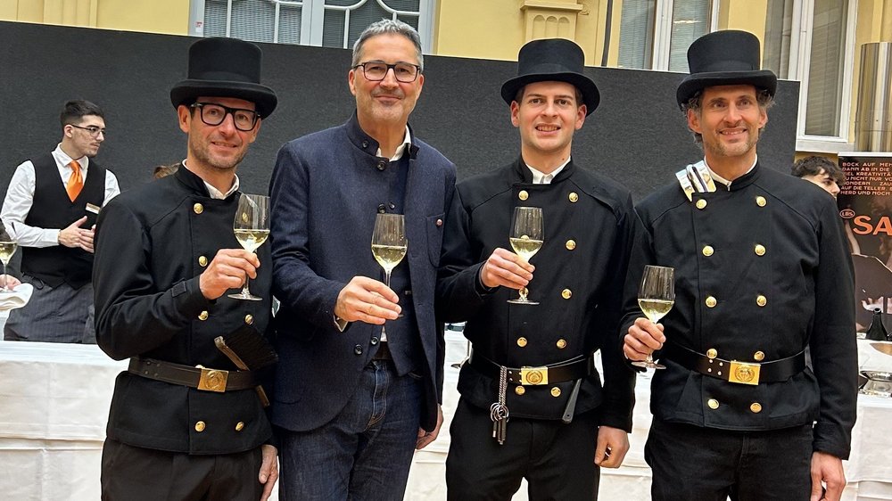 Home Vier Männer, drei in Schornsteinfeger-Uniform, stoßen mit Weingläsern an