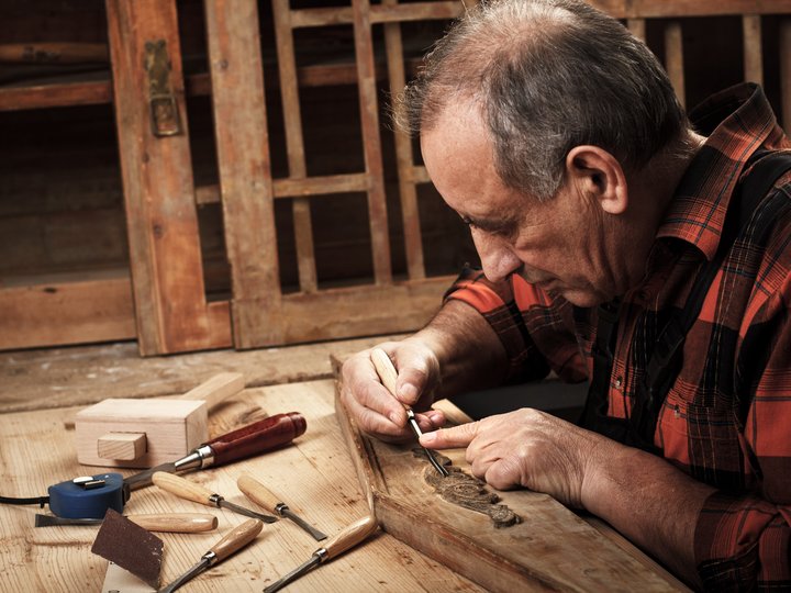 Verzierungsbildhauer Älterer Mann schnitzt Holz auf Werkbank mit Schnitzwerkzeugen