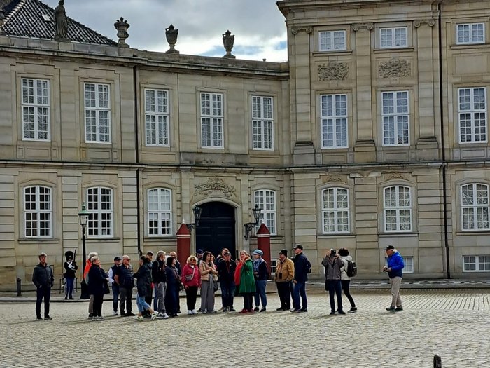 Reisefreudige Althandwerker/innen Gruppe von Touristen vor historischem Gebäude mit steinernem Hof bei bewölktem Himmel