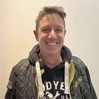 Karosserietechniker Porträt eines lächelnden Mannes mit Jacke und Kapuzenpullover vor weißer Wand