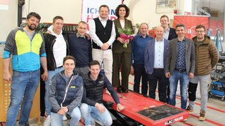 News Gruppenfoto von zwölf Personen in einer Werkstatt, eine Frau hält Blumen