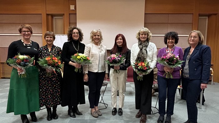 Le donne rafforzano la politica comunale Otto donne in una stanza, cinque tengono mazzi di fiori