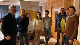 News Sieben Personen stehen vor einem LVH APA Banner in einem Raum mit Holztüren