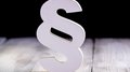 © Daniel Jedzura/Shutterstock.com Weißes Paragraphen-Symbol auf Holzboden vor schwarzem Hintergrund