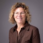 Familiengelder Porträt einer Frau mit lockigen Haaren und Brille vor grauem Hintergrund